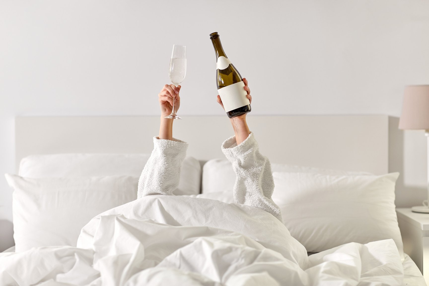 Hands of Woman Lying in Bed with Champagne